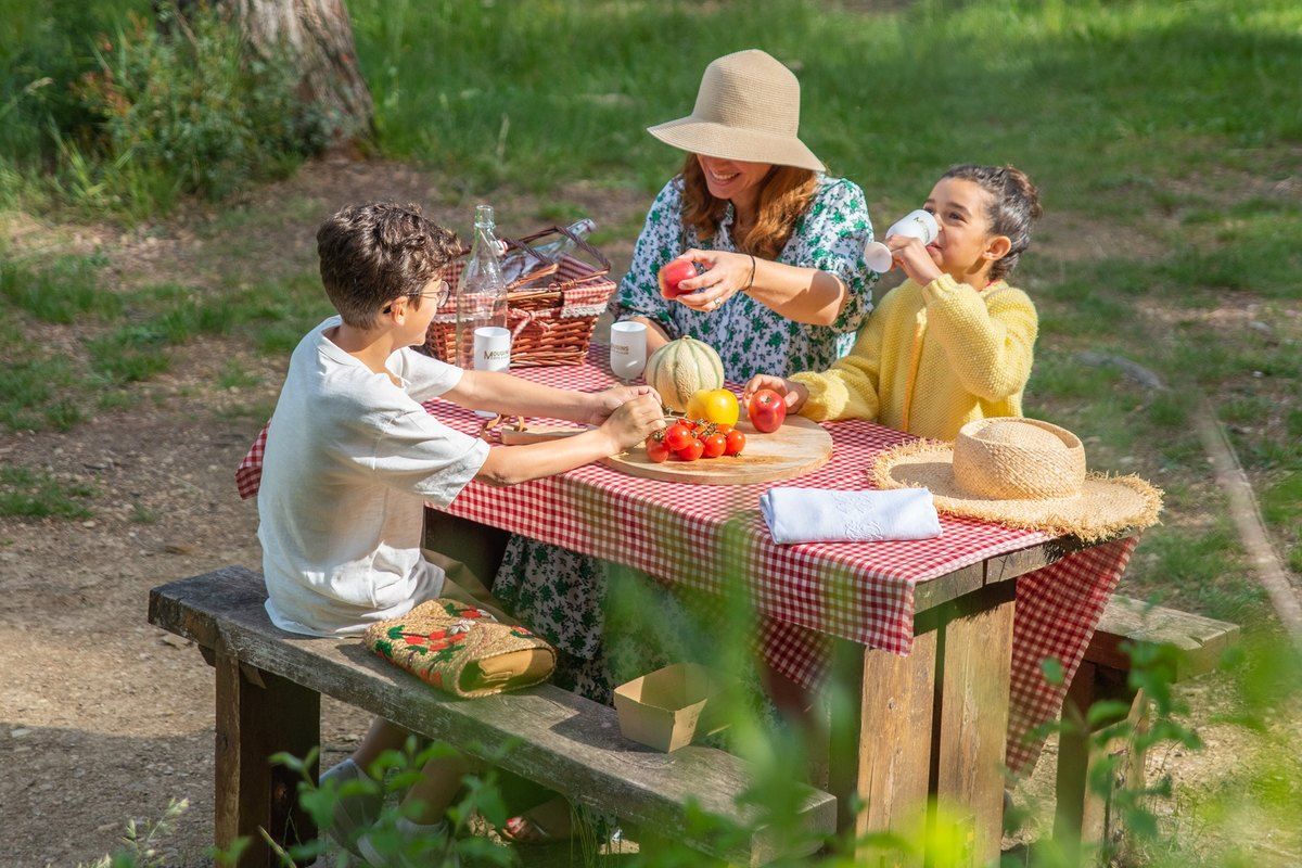 A family picnic at a wooden table under the trees in the Parc de la Valmasque