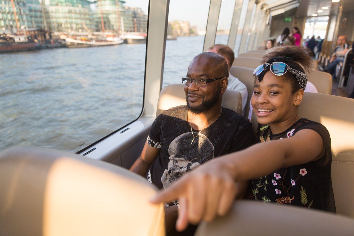 A father and daughter by the window of an Uber Boat by Thames Clippers river bus on the Thames