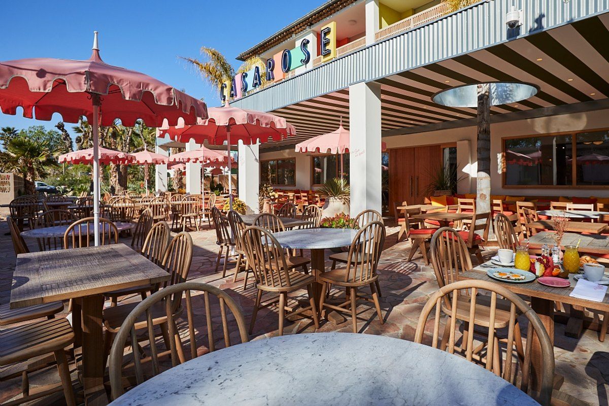 The terrace of the Hôtel Casarose with pink fringed parasols and rattan chairs under palms