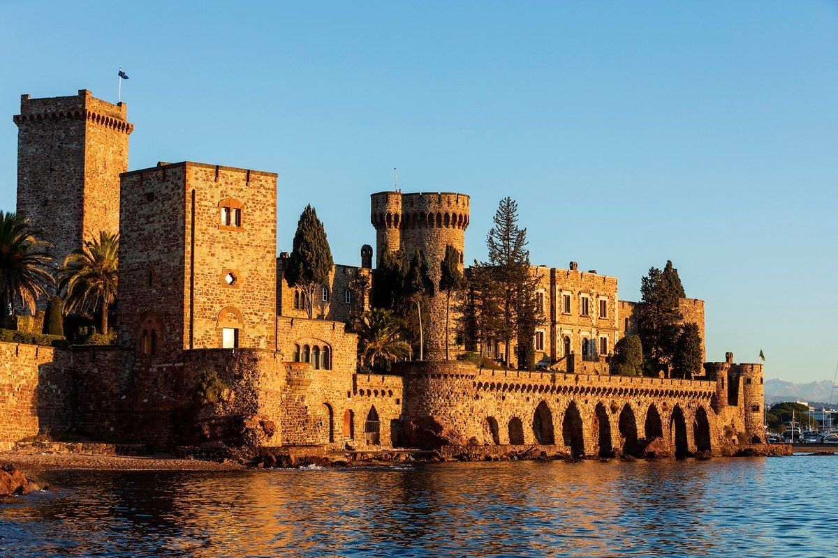 The red-stone towers of the Château de La Napoule rising from the sea in warm evening light