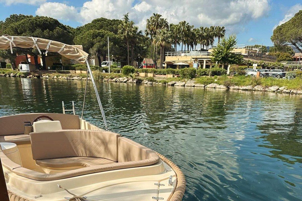 A small wooden electric boat moored on the Siagne river in Mandelieu, palms on the far bank