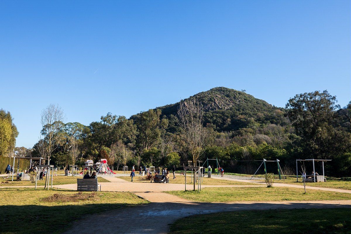 The open lawns, play area and paths of the Parc de l'Argentière in Mandelieu, below a wooded hill