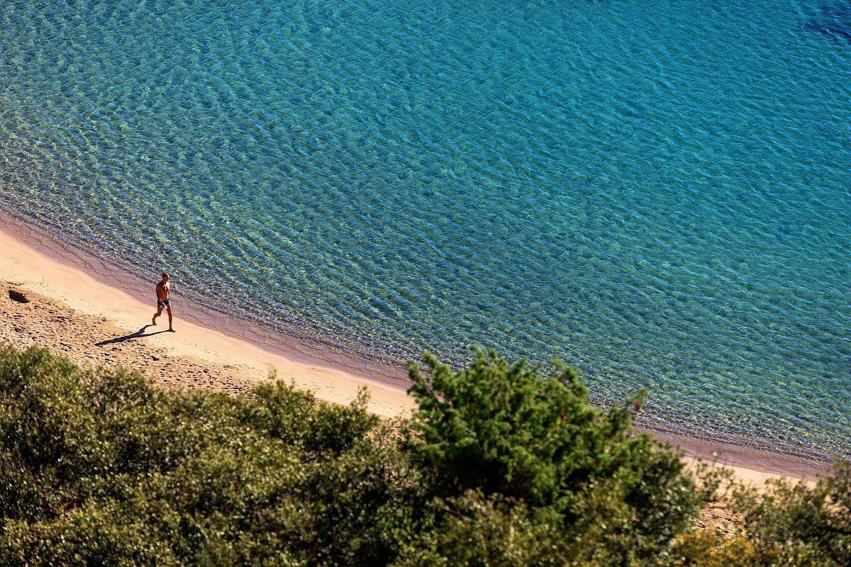 A curve of sand and turquoise water below the red Estérel rocks at La Rague, Mandelieu, seen from above