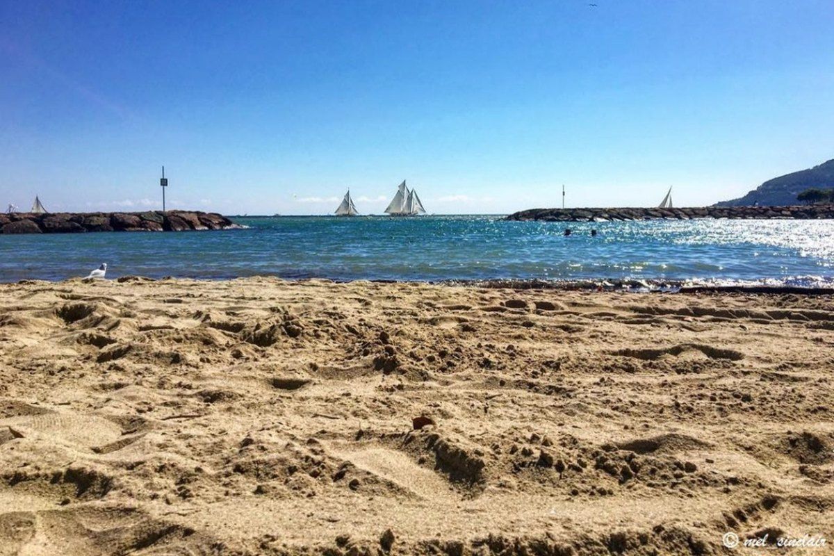 Fine sand on the Plage des Dauphins at Mandelieu, with the harbour wall and sailing boats on the bay