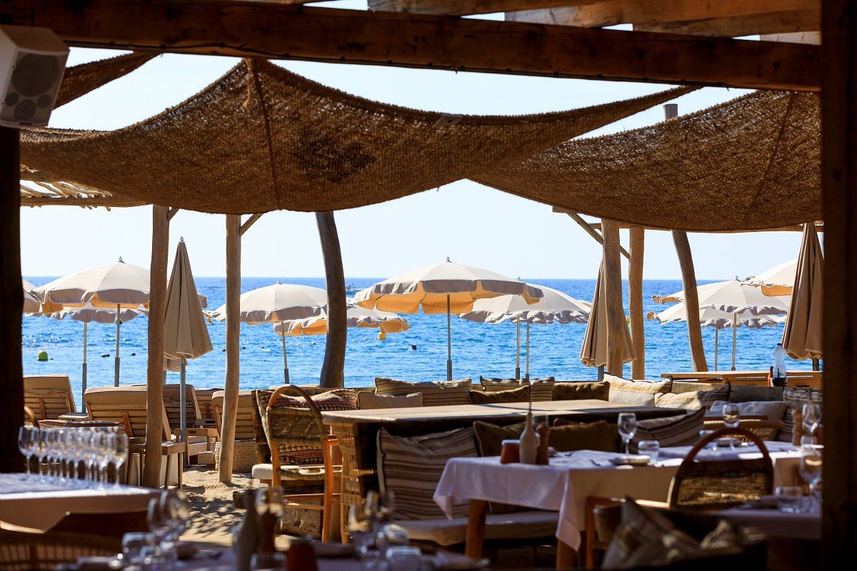 Tables under a reed awning at Playa Chica, with parasols and the sea beyond