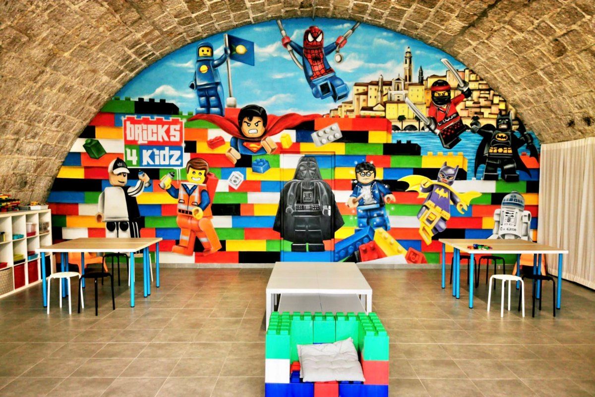 The vaulted Bricks 4 Kidz workshop on the Sablettes esplanade, with a LEGO mural and children's tables