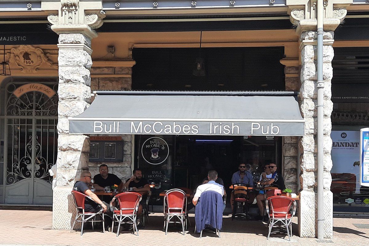 Drinkers at the pavement tables of Bull McCabe's Irish pub in a Belle Époque building in Menton
