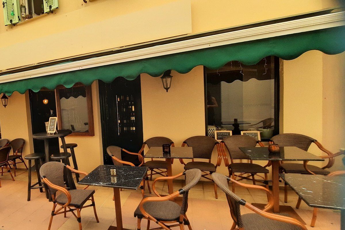 The covered terrace of Persephone café-bar under a green awning on rue de la Marne, Menton