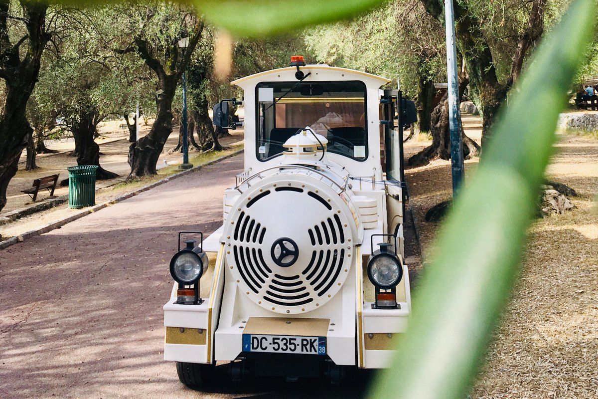 The white petit train touristique of Menton on a tree-lined promenade