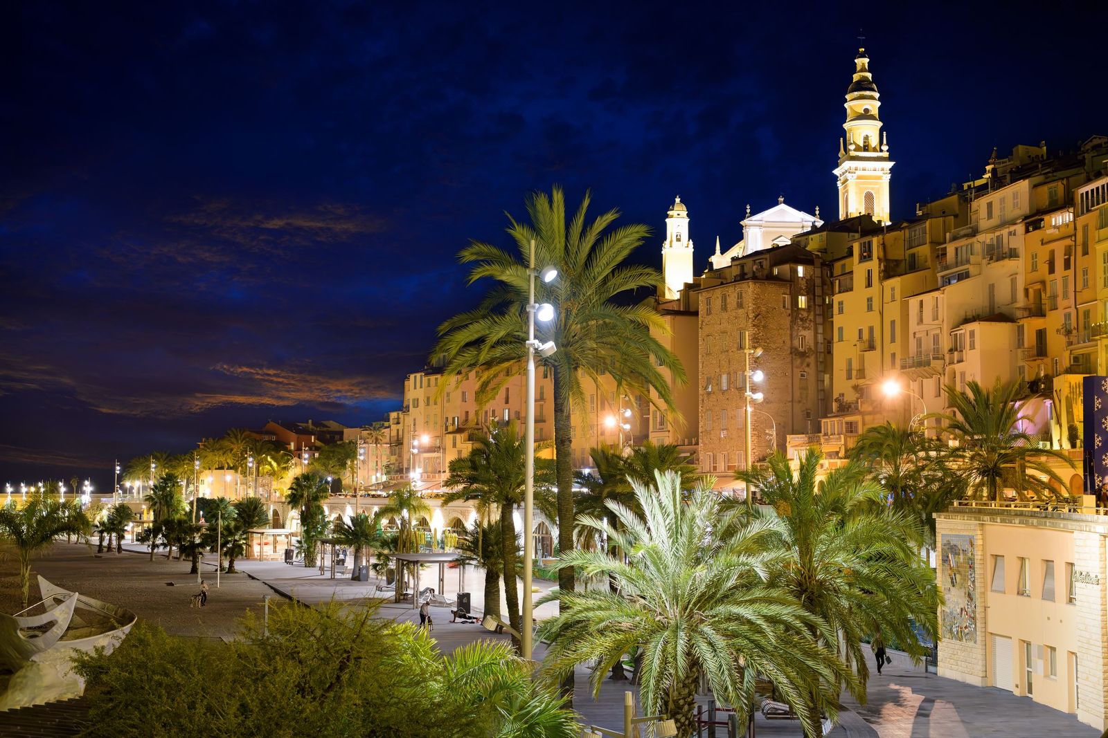 The Promenade de la Mer lit up at night, with the Basilica of Saint-Michel above the old town