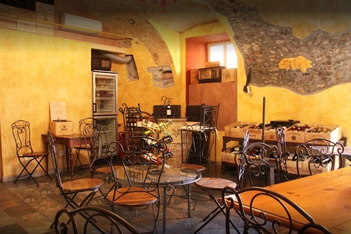 The ochre vaulted room of Vinum Veritas wine bar in Menton's old town, with bistro tables and wine cases
