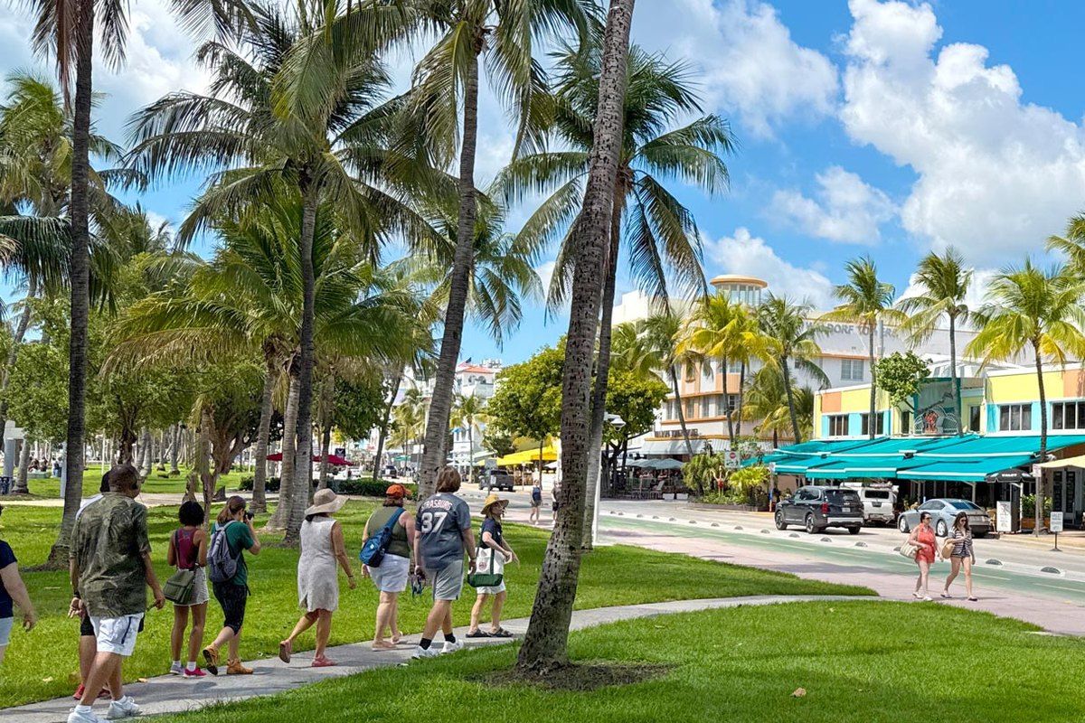 A walking-tour group on the palm-lined path of Lummus Park with Art Deco hotels on Ocean Drive behind
