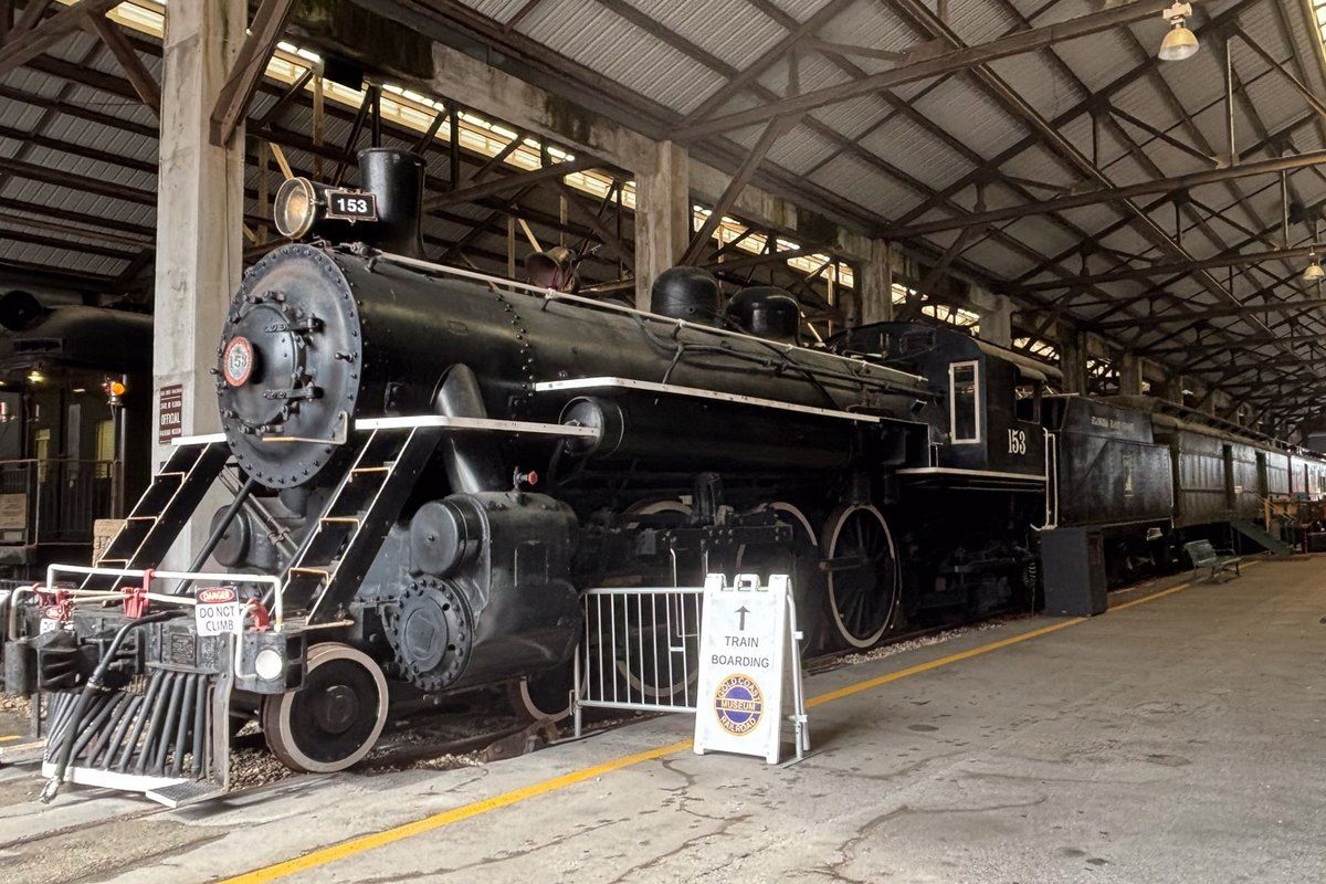 A black steam locomotive under the train shed at the Gold Coast Railroad Museum