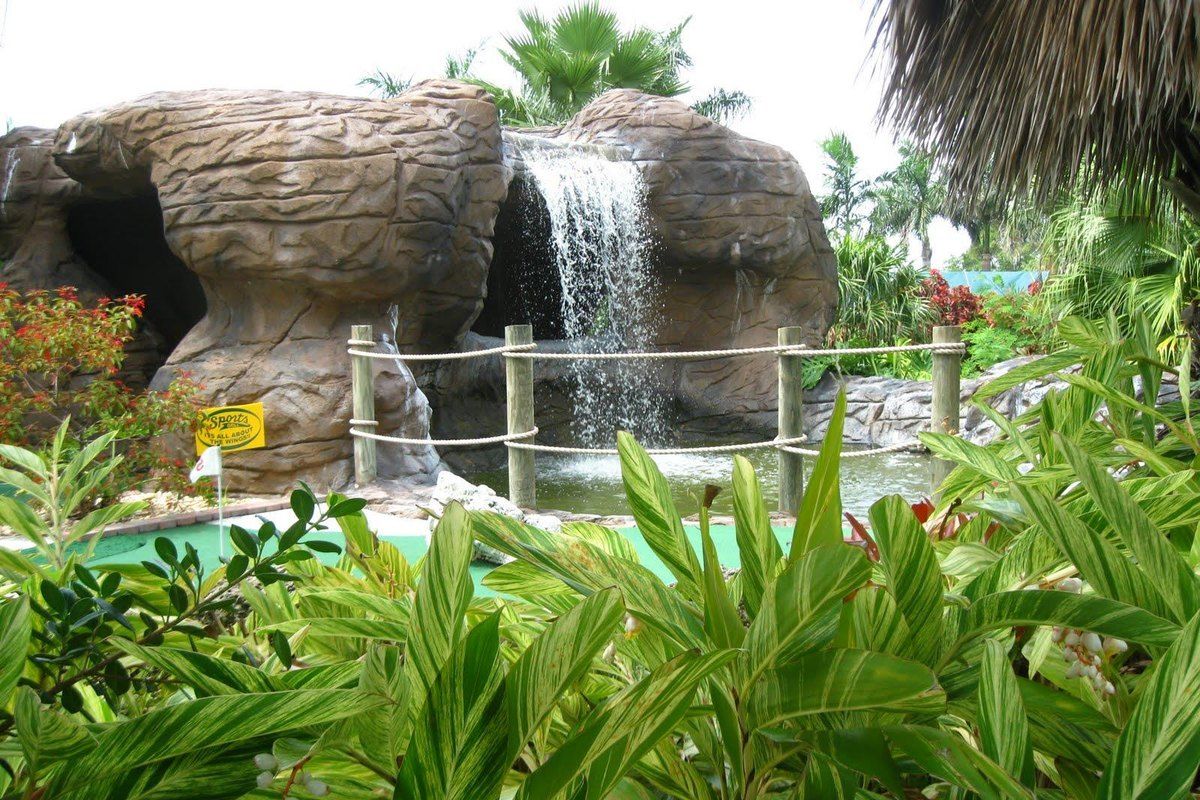 A waterfall tumbling over an artificial rock cave beside the greens of Palmetto Mini Golf