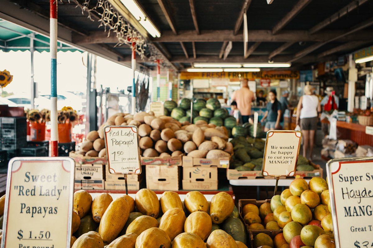 Crates of papayas, mangoes and coconuts with hand-written price signs under the roof of the Robert Is Here fruit stand