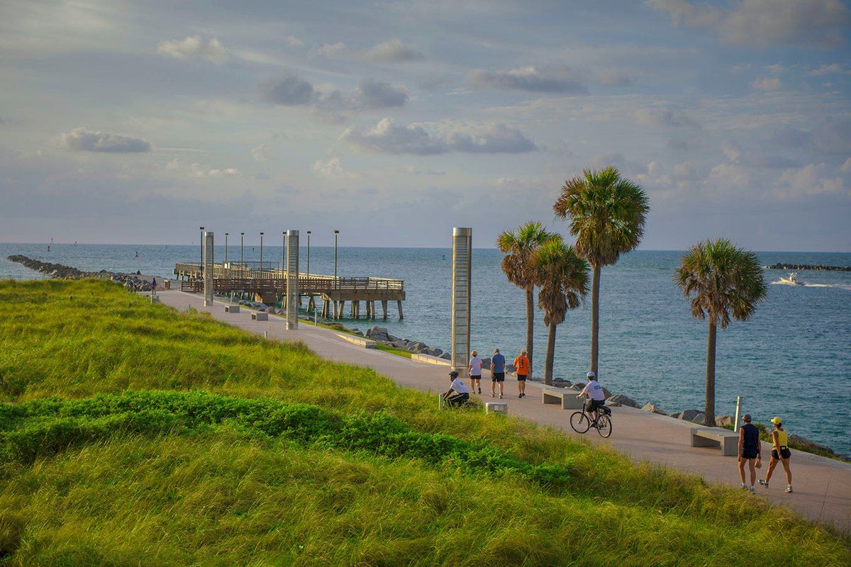 Grassy dunes, palms and the promenade leading to the pier at South Pointe Park, Miami Beach, in evening light