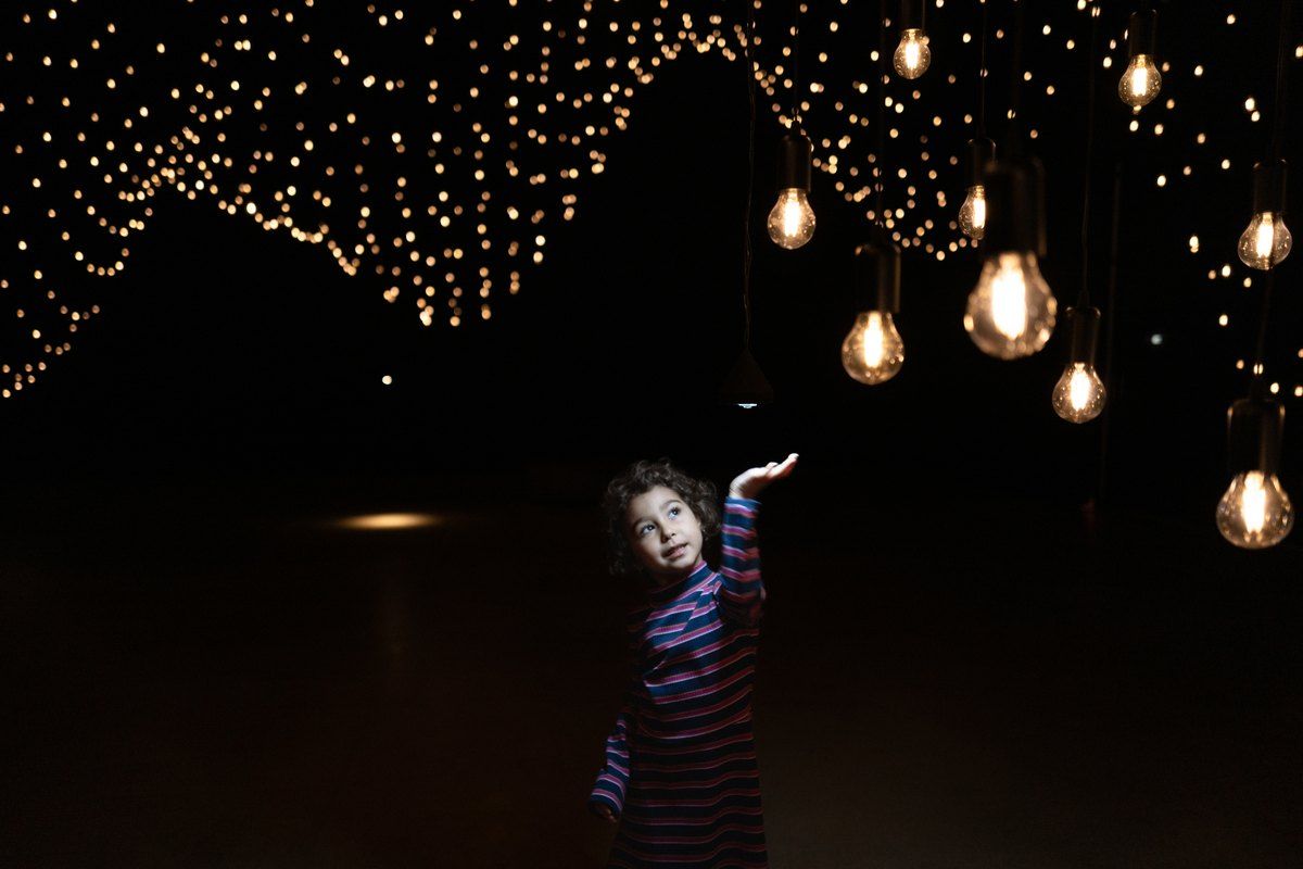 A child reaching up towards thousands of glowing light bulbs in Pulse Topology at Superblue Miami