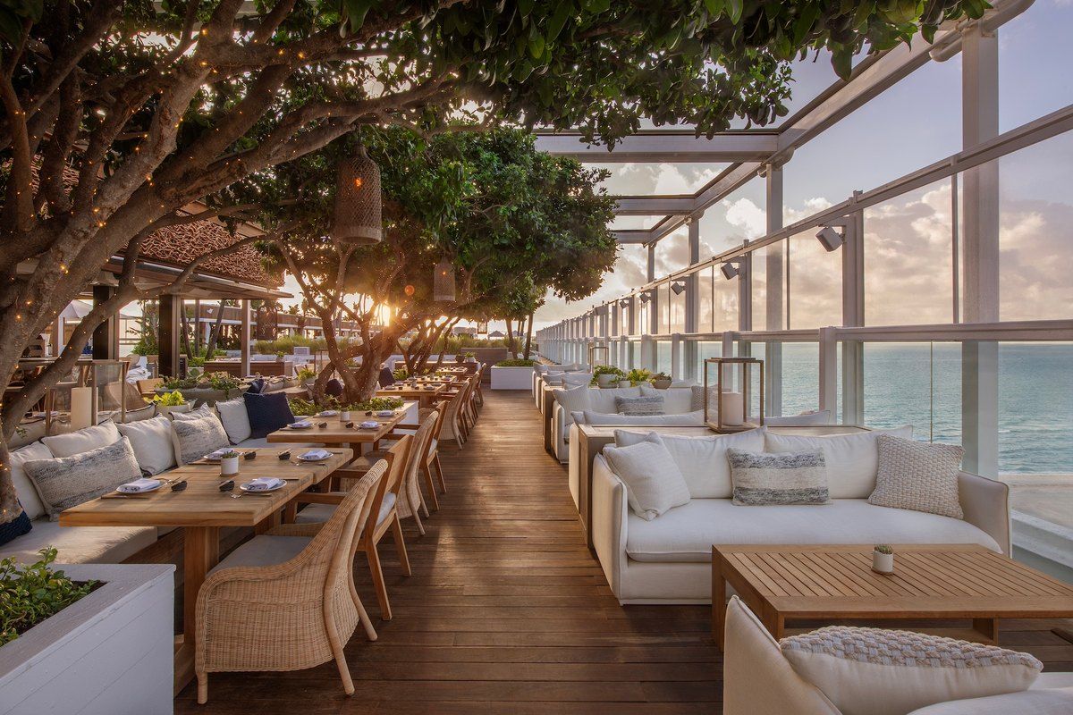 Sofas and tables under trees on the ocean-facing rooftop terrace of Watr at the 1 Hotel South Beach