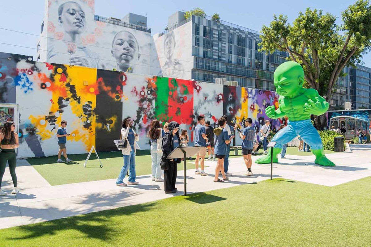 Visitors among murals and a giant green figure sculpture on the lawn at Wynwood Walls