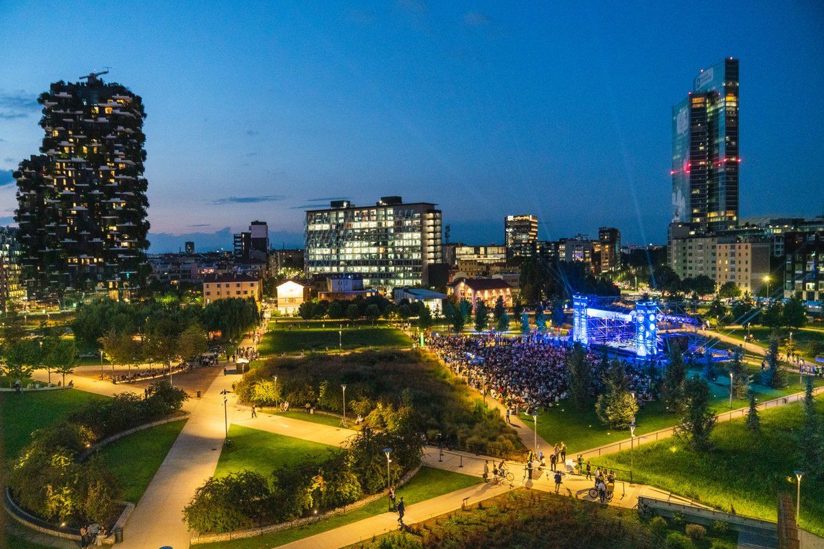 BAM – Biblioteca degli Alberi at dusk, its lawns and paths lit beneath the Porta Nuova towers