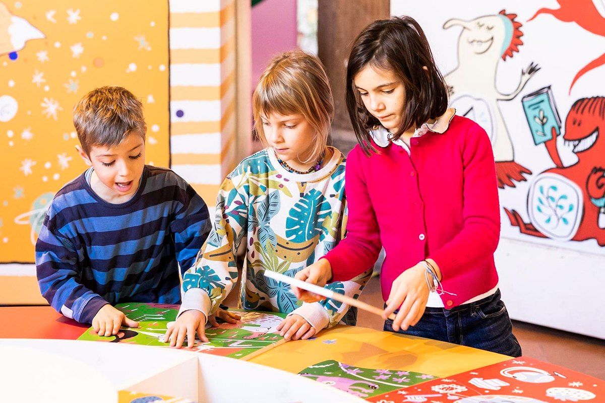 Three children playing with a colourful board in a MUBA exhibition room at the Rotonda della Besana, Milan