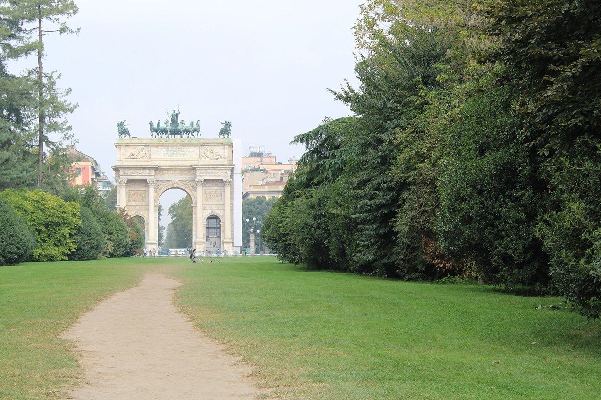 A path through the lawns and trees of Parco Sempione leading to the Arco della Pace