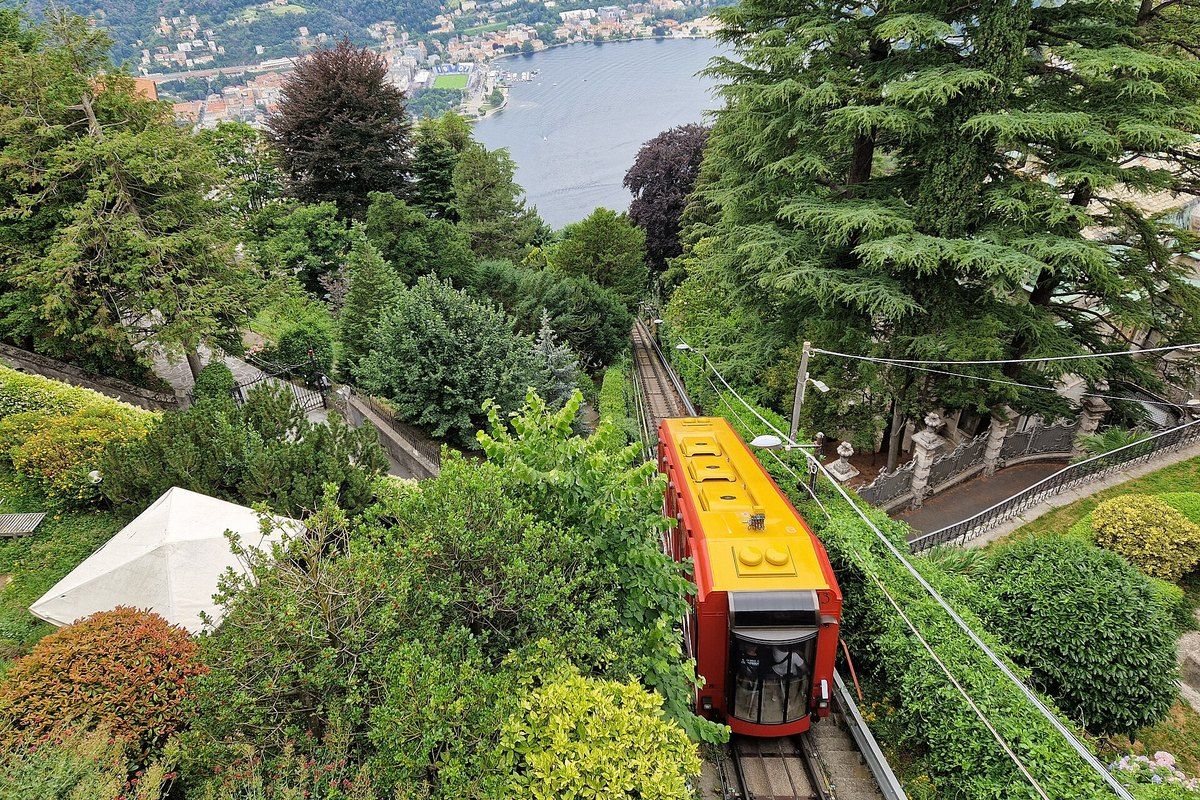 The red Como–Brunate funicular car descending through gardens towards Como and the lake
