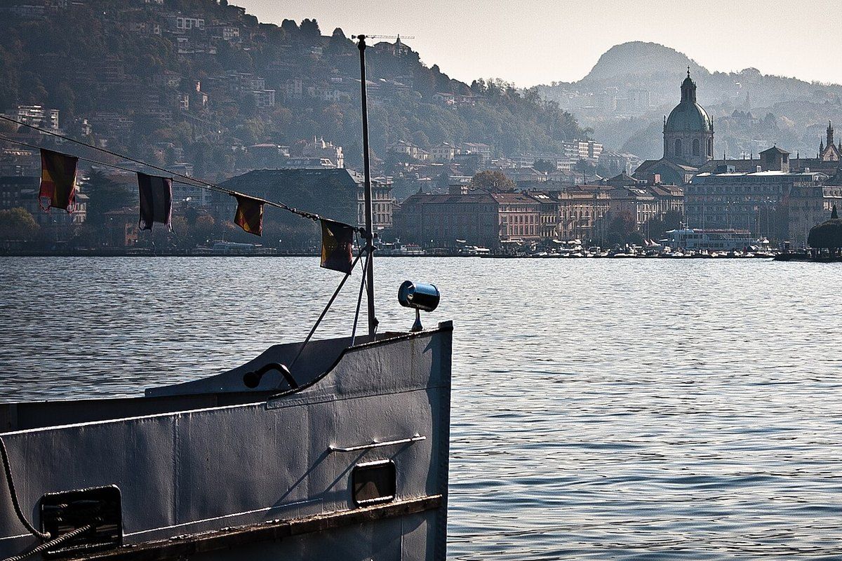 The bow of a Lake Como passenger boat with the Como waterfront and cathedral dome behind