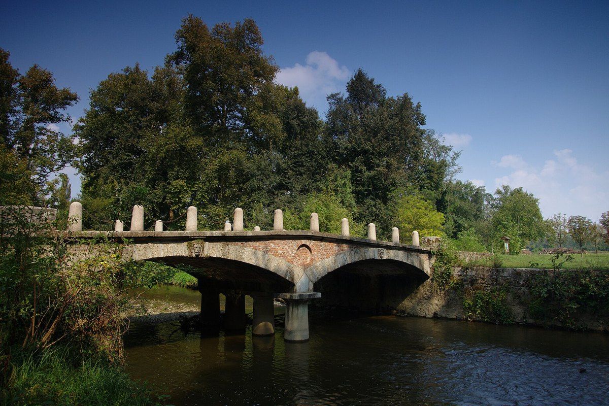 An old stone bridge over the Lambro river among the trees of the Parco di Monza