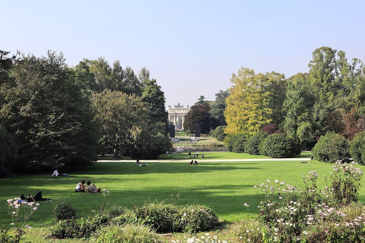 Lawns, flower beds and tall trees in Parco Sempione with the Arco della Pace in the distance