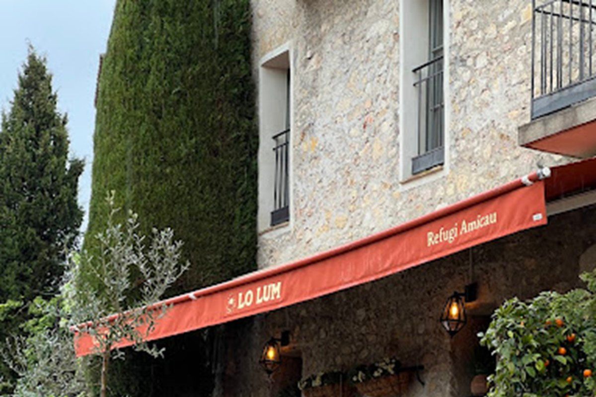 Rattan chairs under the red awning of Lo Lum on the cobbles of Place des Patriotes in Mougins
