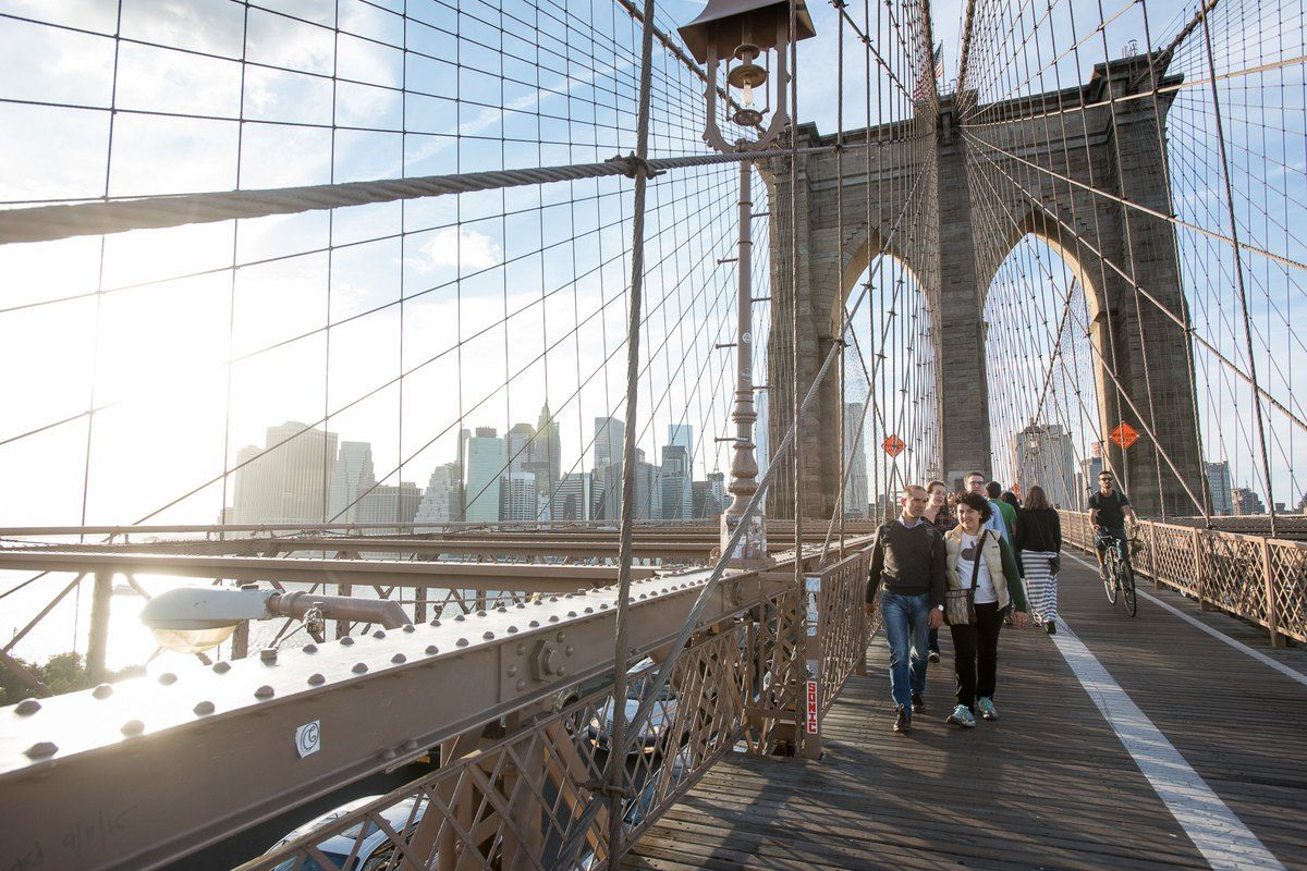 Walkers on the Brooklyn Bridge promenade beneath the stone tower and cables