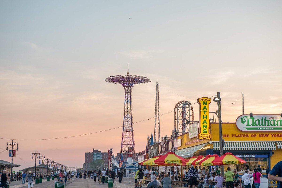 The Riegelmann Boardwalk at Coney Island at sunset, with the Parachute Jump and Nathan's Famous