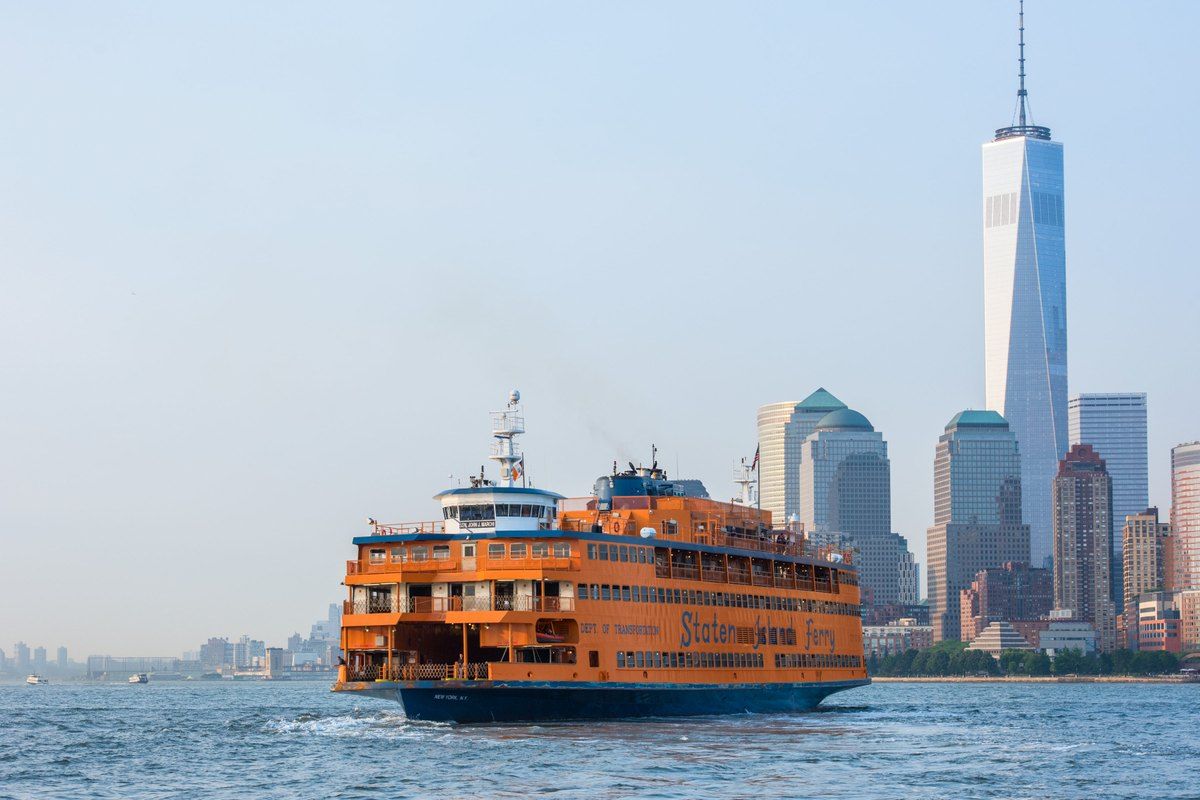 An orange Staten Island Ferry crossing the harbour with One World Trade Center and Lower Manhattan behind