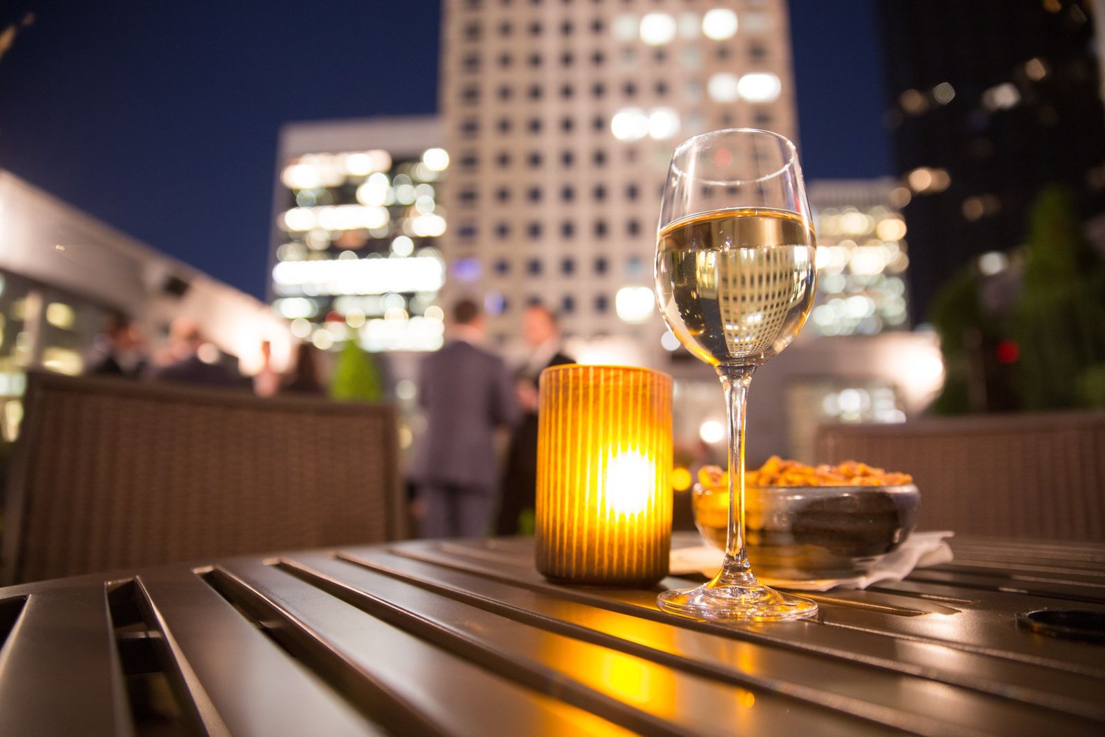 A glass of white wine and a candle, with the city lit up behind