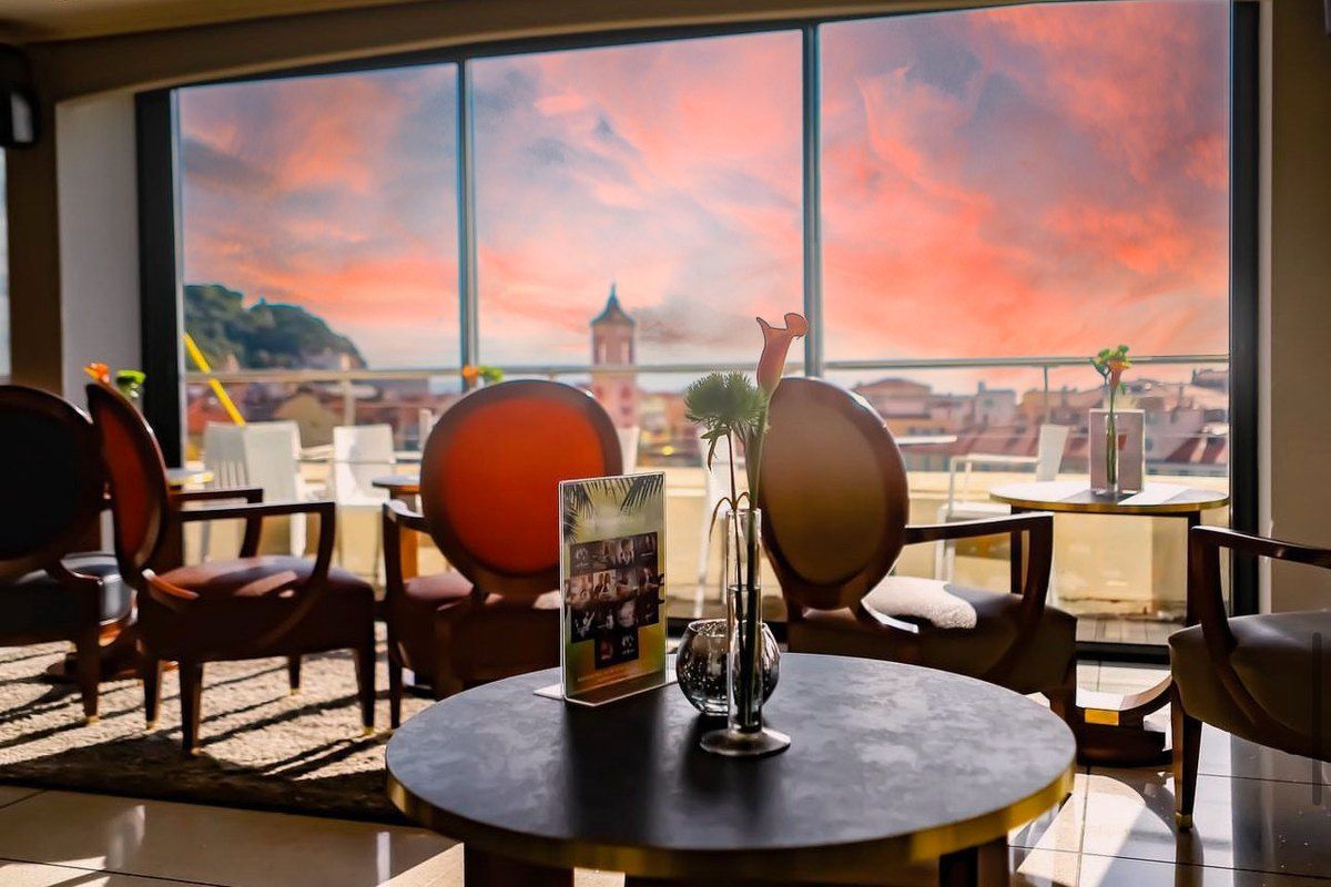 Armchairs by the picture windows of the Moon Bar at the Aston La Scala, with a pink evening sky over Vieux Nice