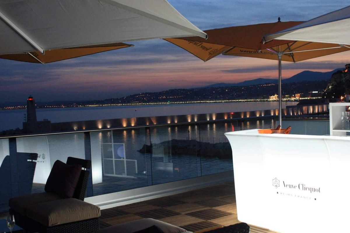 The rooftop bar of La Réserve de Nice at dusk, with the port lighthouse and the lights of the Baie des Anges behind
