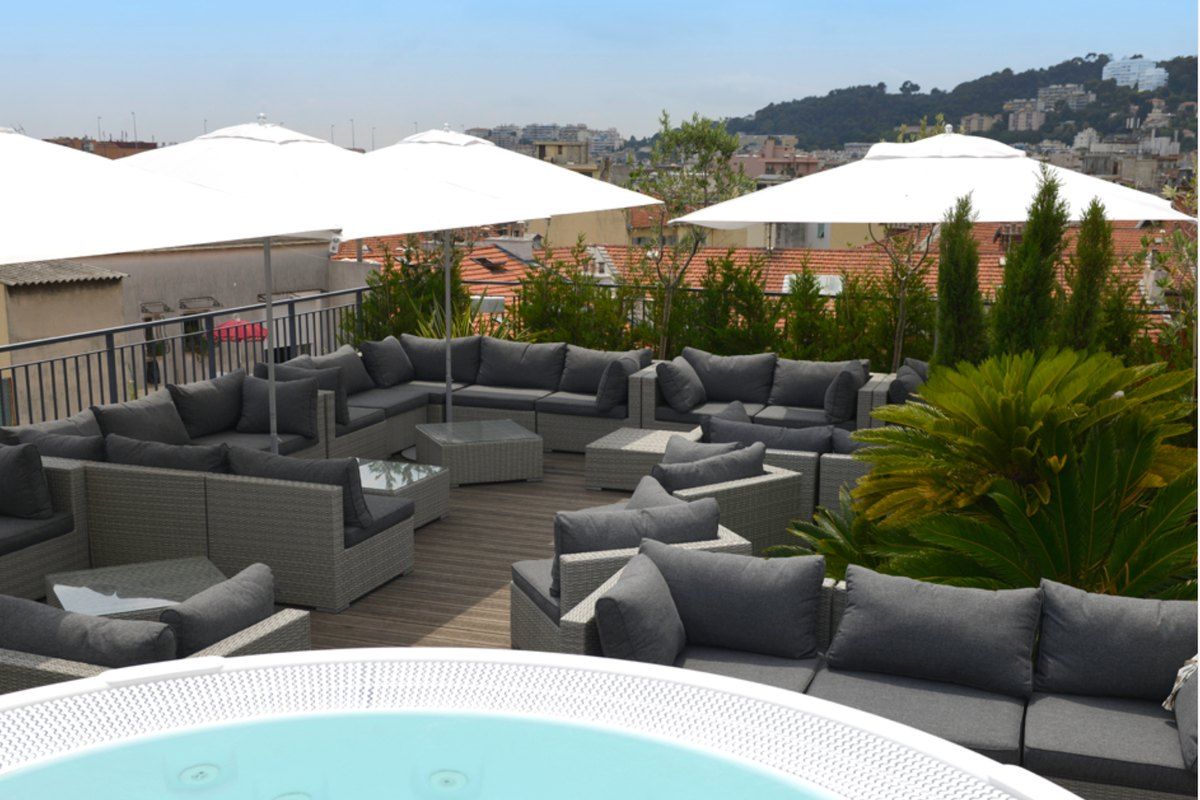 Lounge sofas, parasols and a hot tub on the Rooftop Monsigny above central Nice, with the hills behind