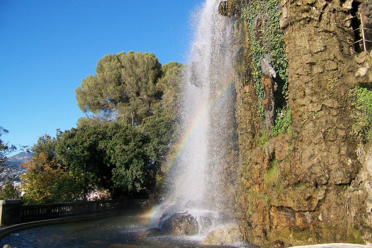 The waterfall on Castle Hill in Nice, falling past pines under a blue sky