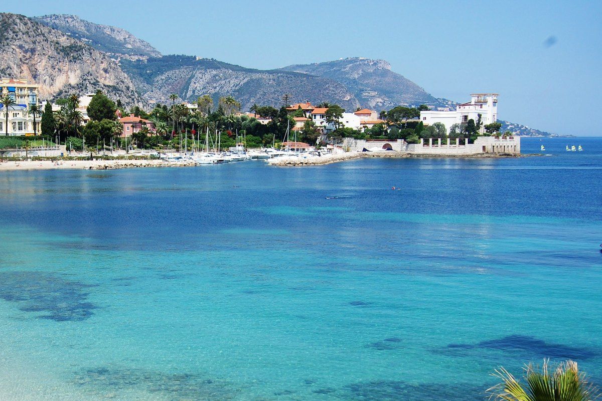 Clear turquoise water in the Baie des Fourmis at Beaulieu-sur-Mer, with villas and mountains behind