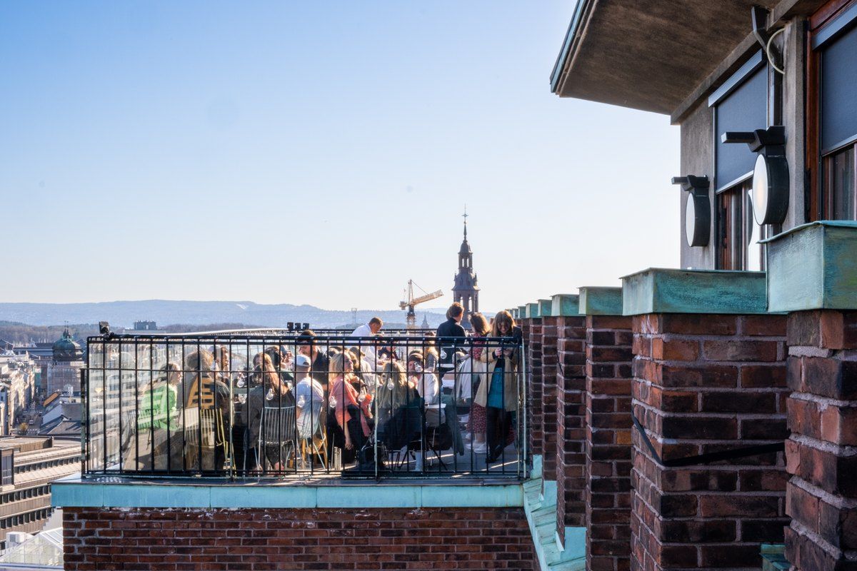 People on the Byens Tak roof terrace atop the Folketeater building, with Oslo's rooftops and spires beyond