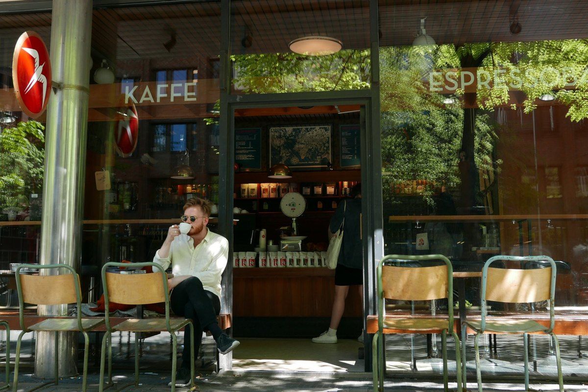 A man with a coffee at the pavement tables outside Fuglen's glass front, with its red bird sign