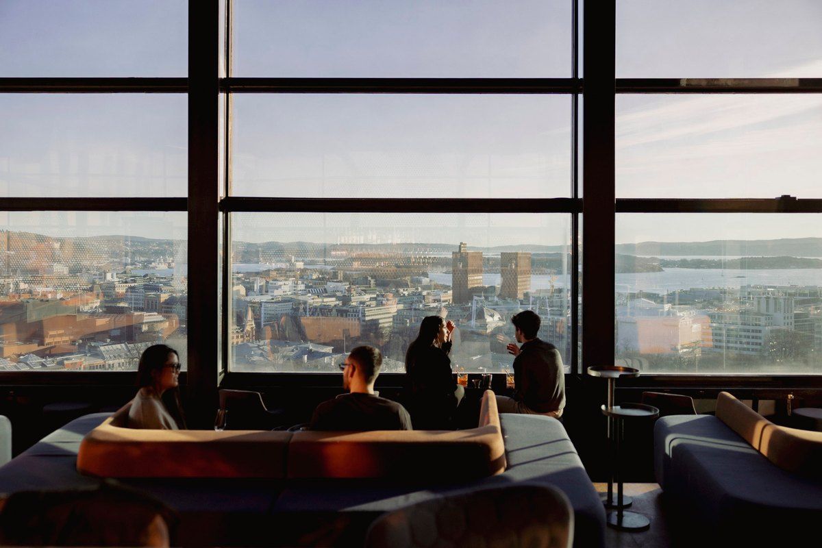 Guests in low lounge seating at Summit Bar on the 21st floor, with Oslo and the fjord through the tall windows