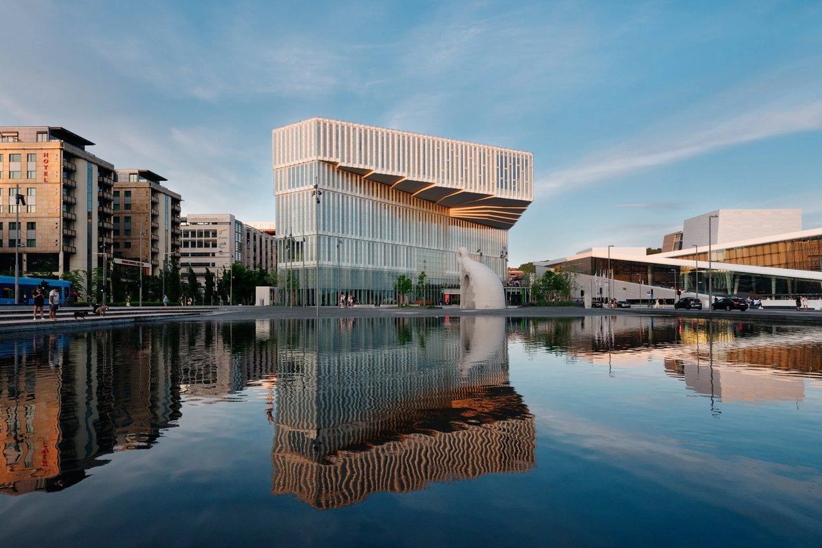 The Deichman Bjørvika library building reflected in still water under a blue sky in Oslo