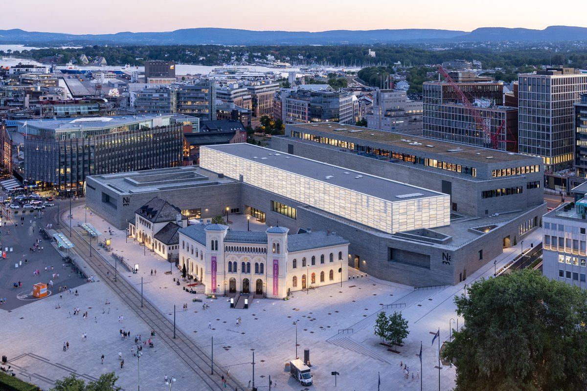 The National Museum in Oslo seen from above at dusk, with its lit rooftop hall above the harbour district