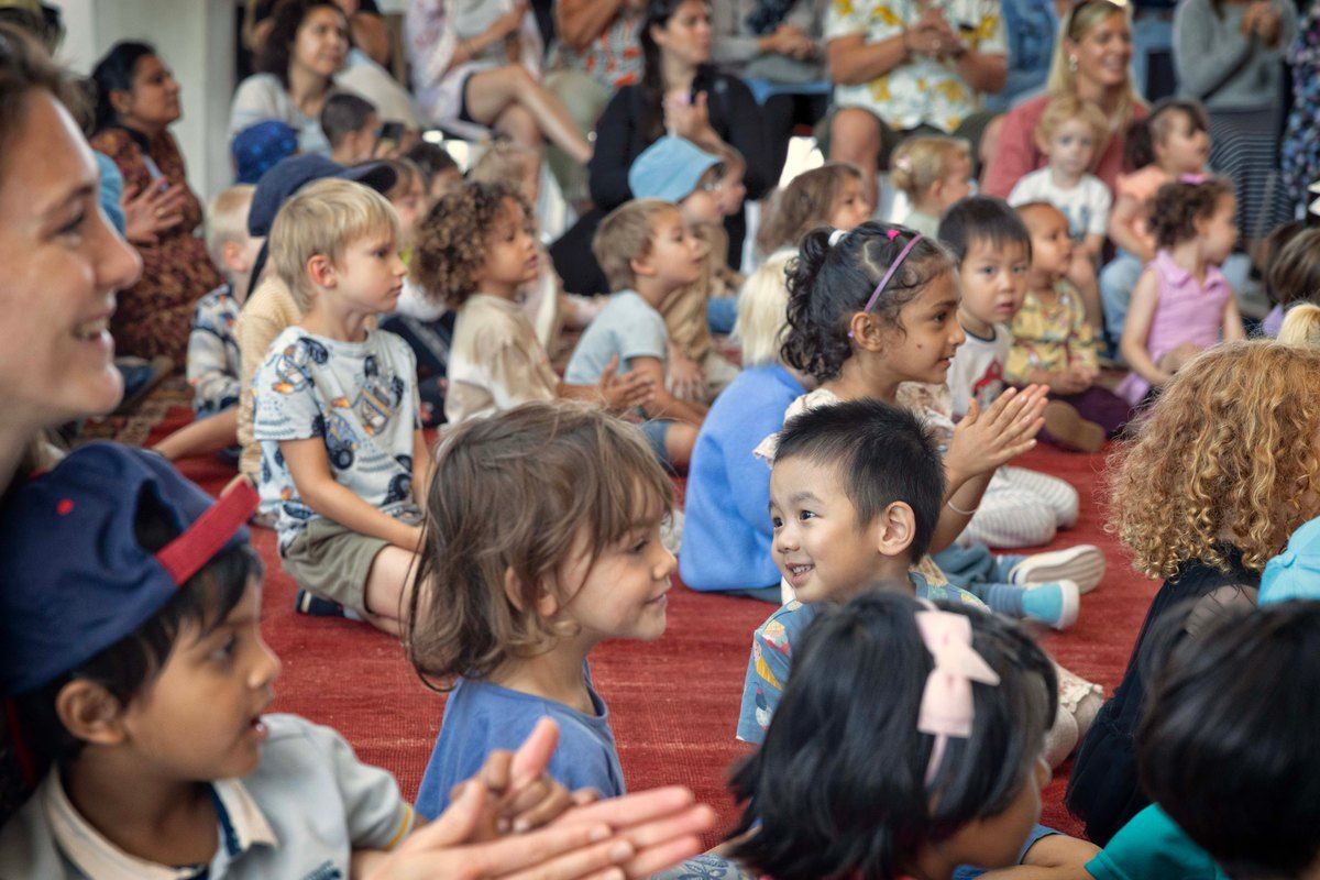 Small children and parents sitting on a red carpet clapping during Saturday Song in the foyer of the Oslo Opera House