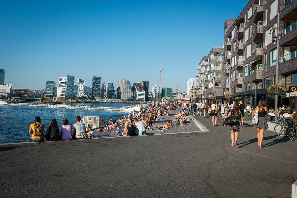 People strolling and sitting by the water on the harbour promenade at Sørenga, looking towards the Barcode towers