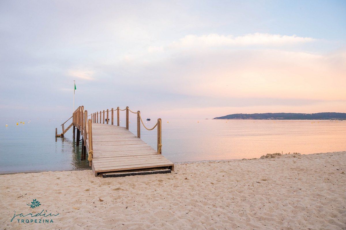 A wooden jetty running out from the sand at Jardin Tropézina on the Baie de Pampelonne at dusk
