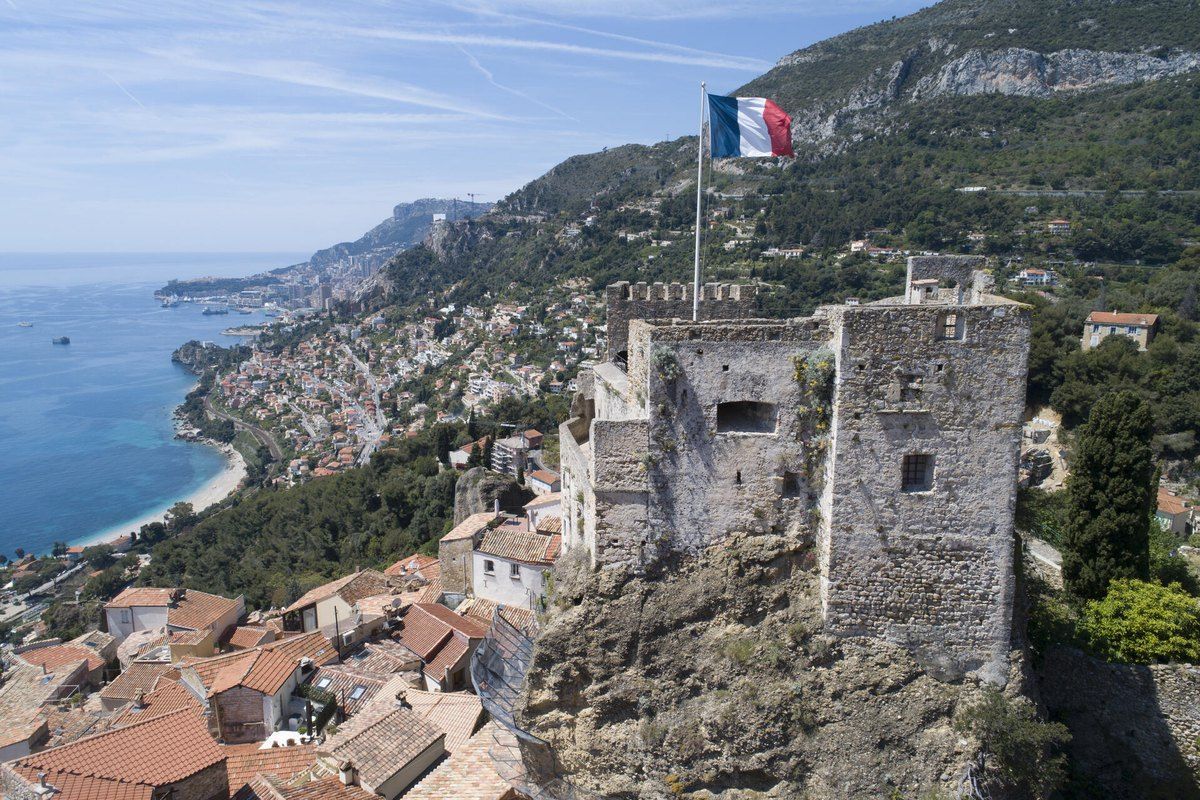 The 10th-century keep of Roquebrune's medieval castle with the French flag, above the village rooftops and the coast to Monaco