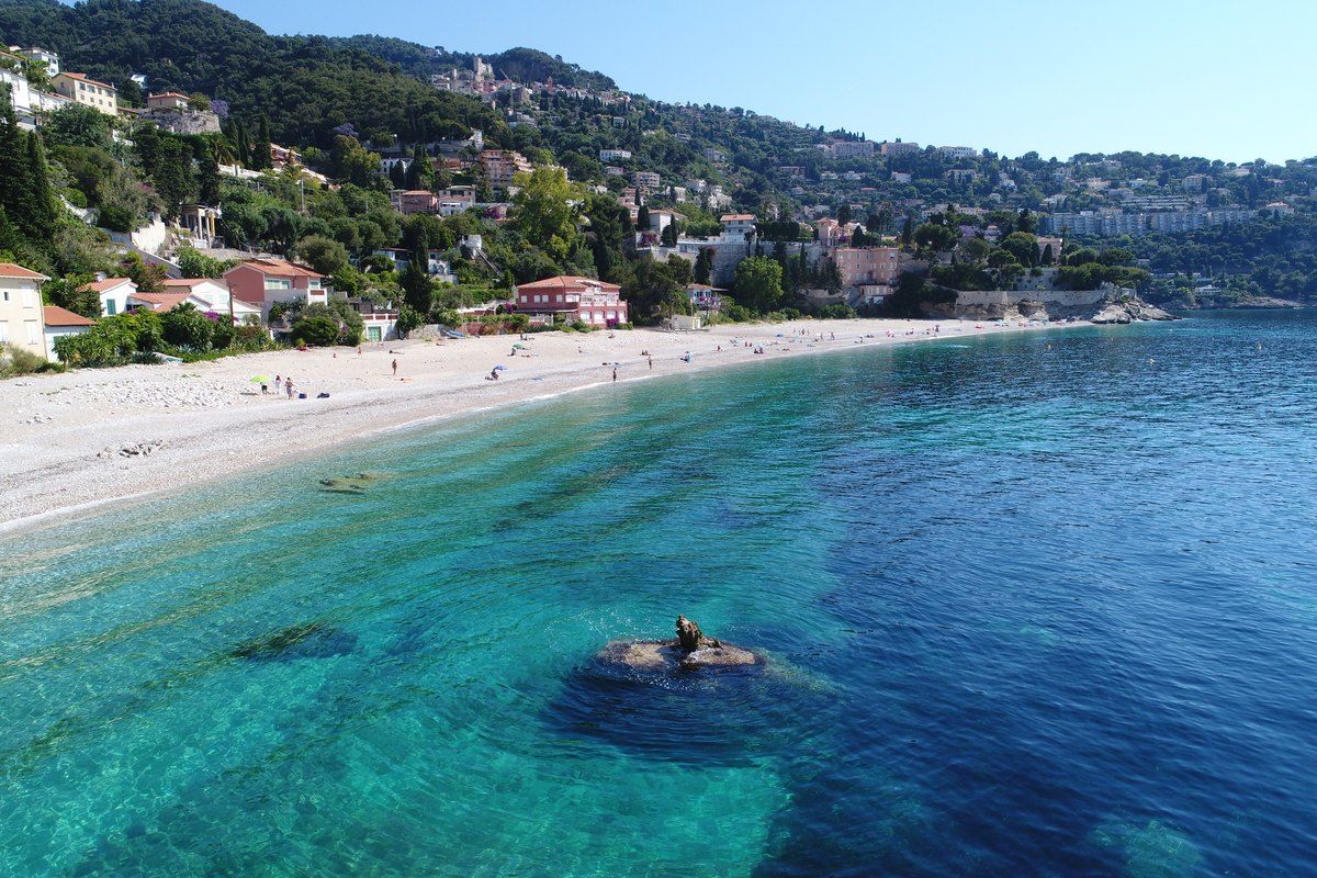 The long pebble crescent of Plage du Golfe Bleu and its clear turquoise water below wooded hills at Roquebrune-Cap-Martin